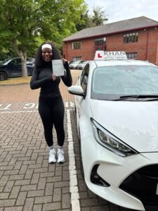 Barbara holding her driving test pass certificate next to Khan School of Motoring car in Slough