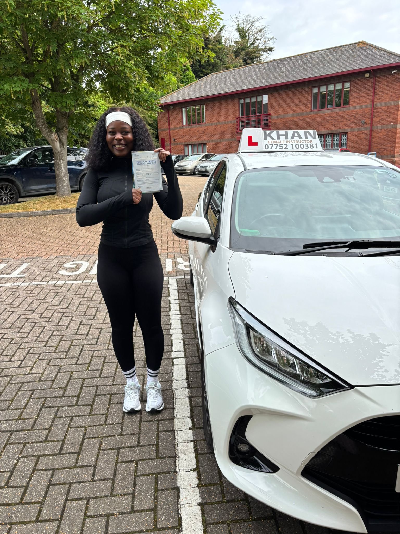 Barbara holding her driving test pass certificate next to Khan School of Motoring car in Slough