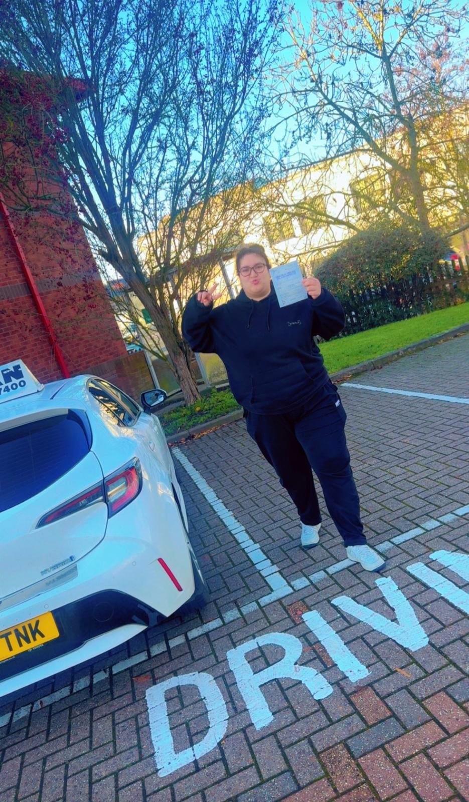 Jade holding her driving test pass certificate next to Khan School of Motoring car in Slough
