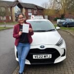 Kiran holding her driving test pass certificate next to Khan School of Motoring car in Slough