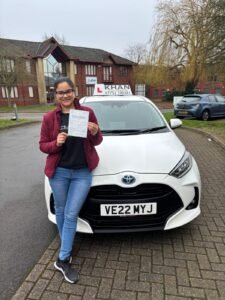 Kiran holding her driving test pass certificate next to Khan School of Motoring car in Slough