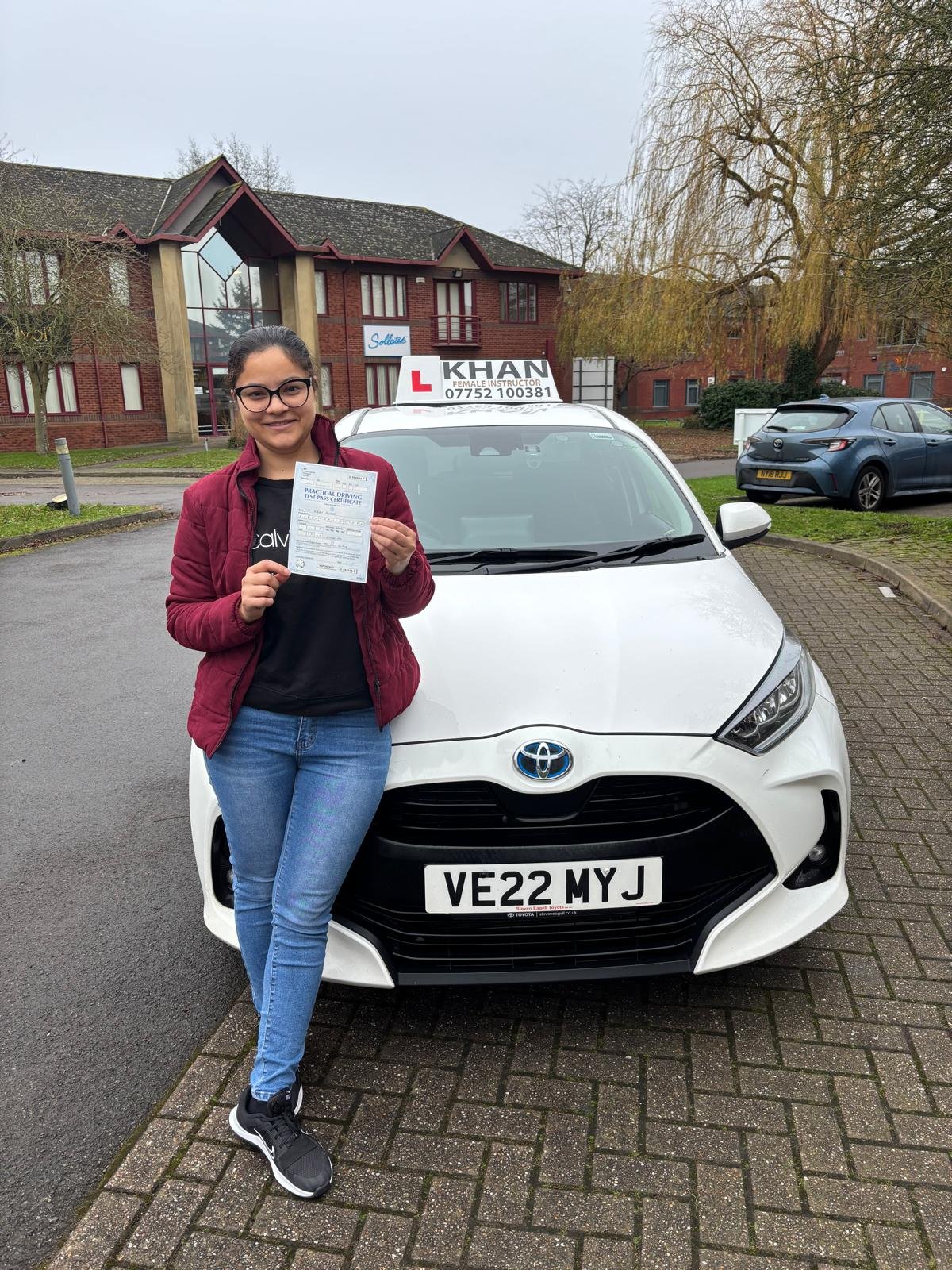 Kiran holding her driving test pass certificate next to Khan School of Motoring car in Slough