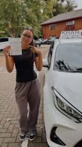 Laiba holding her driving test pass certificate next to Khan School of Motoring car in Slough