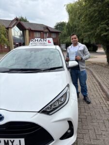 Mayank holding his driving test pass certificate next to Khan School of Motoring car in Slough