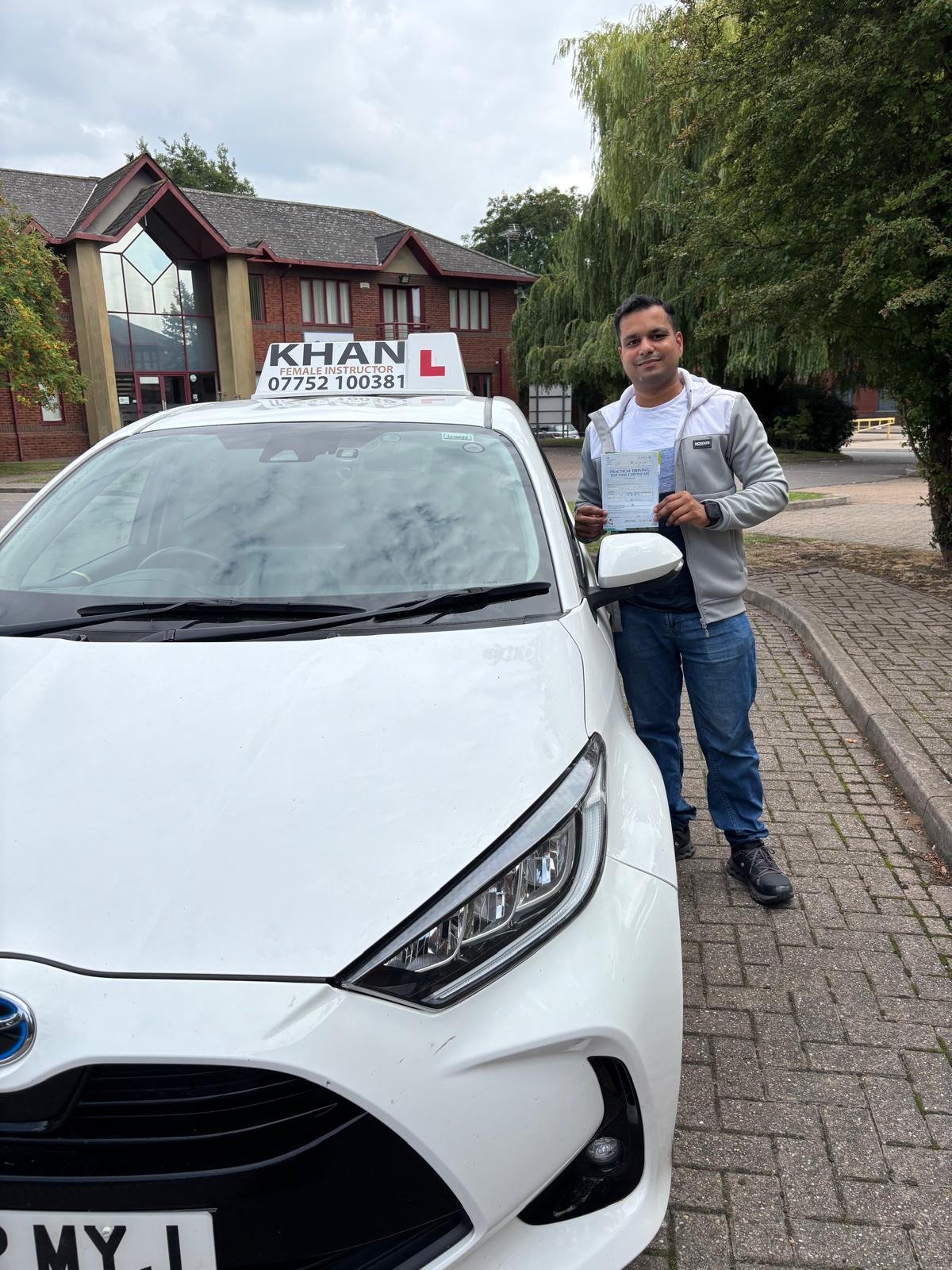 Mayank holding his driving test pass certificate next to Khan School of Motoring car in Slough