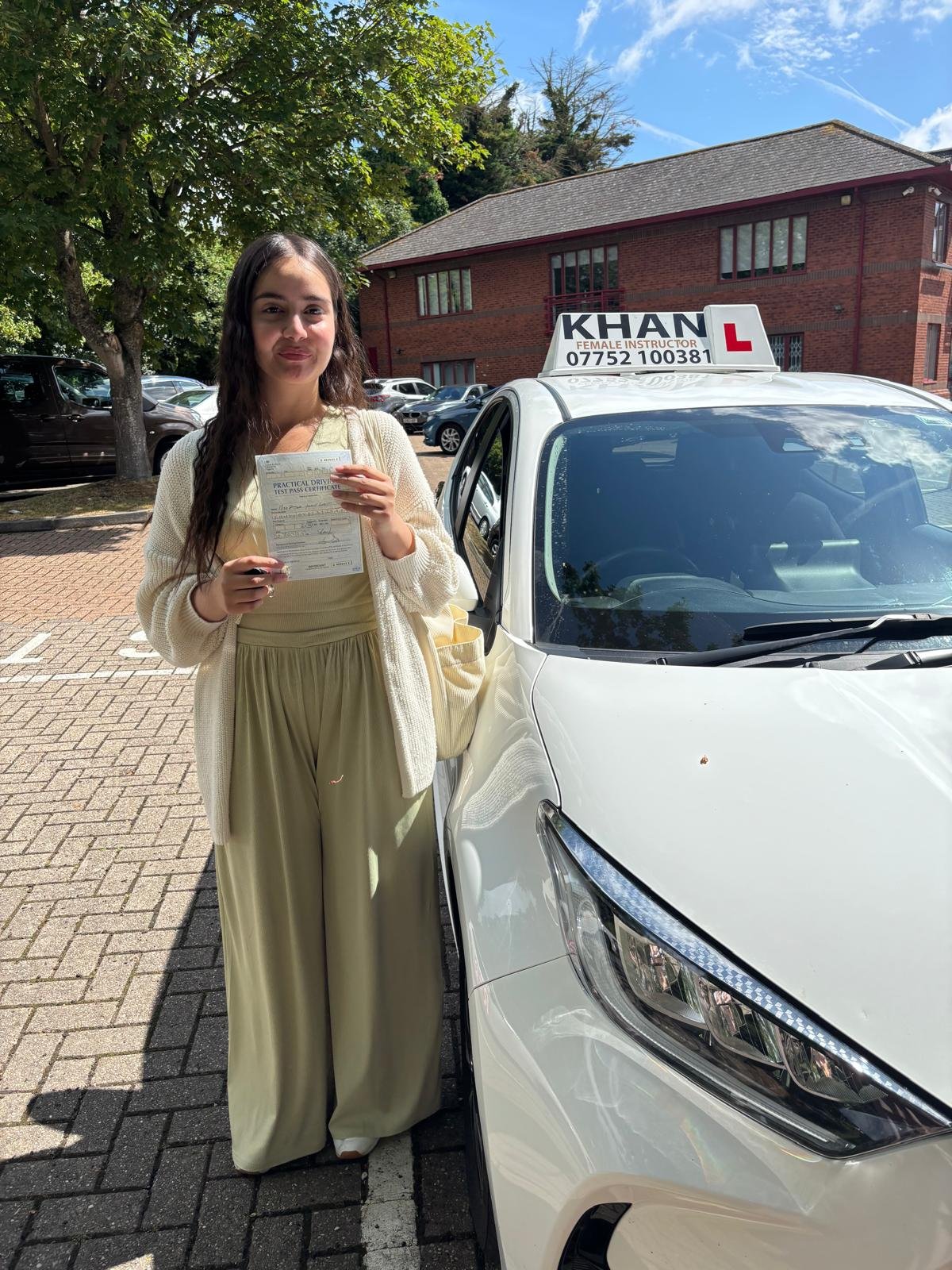 Nabeela holding her driving test pass certificate next to Khan School of Motoring car in Slough