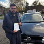 Naveen holding his driving test pass certificate next to Khan School of Motoring car in Slough