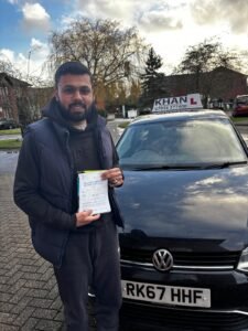 Naveen holding his driving test pass certificate next to Khan School of Motoring car in Slough