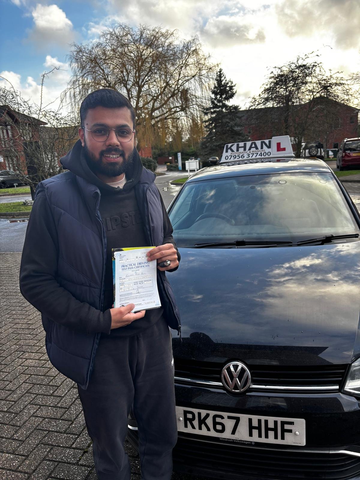 Naveen holding his driving test pass certificate next to Khan School of Motoring car in Slough