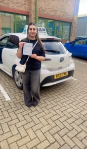 Rabia holding her driving test pass certificate next to Khan School of Motoring car in Slough