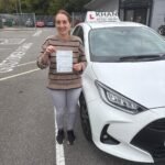 Saima holding her driving test pass certificate next to Khan School of Motoring car in Slough