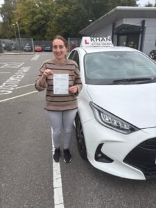 Saima holding her driving test pass certificate next to Khan School of Motoring car in Slough