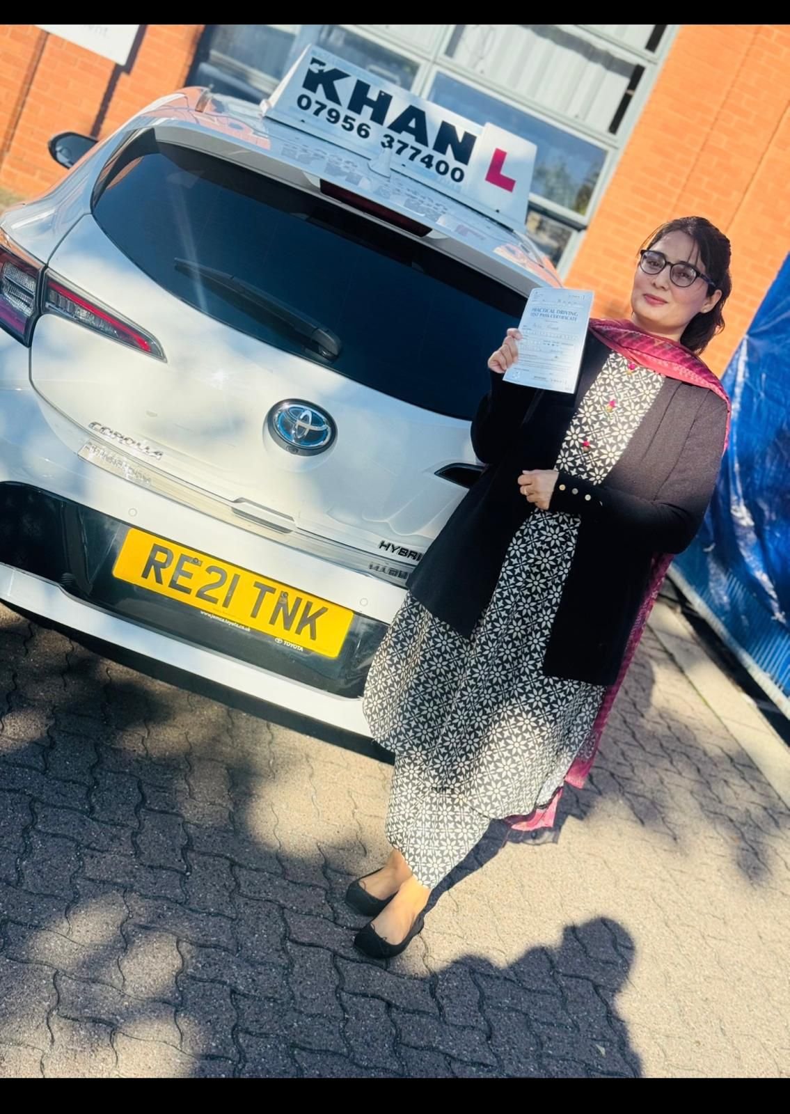 Shamila holding her driving test pass certificate next to Khan School of Motoring car in Slough