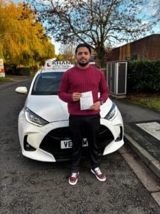 Shrican holding his driving test pass certificate next to Khan School of Motoring car in Slough