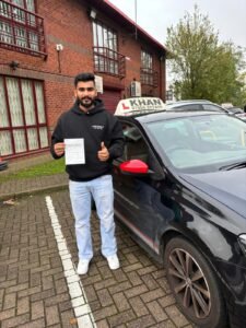 Sunjat holding his driving test pass certificate next to Khan School of Motoring car in Slough