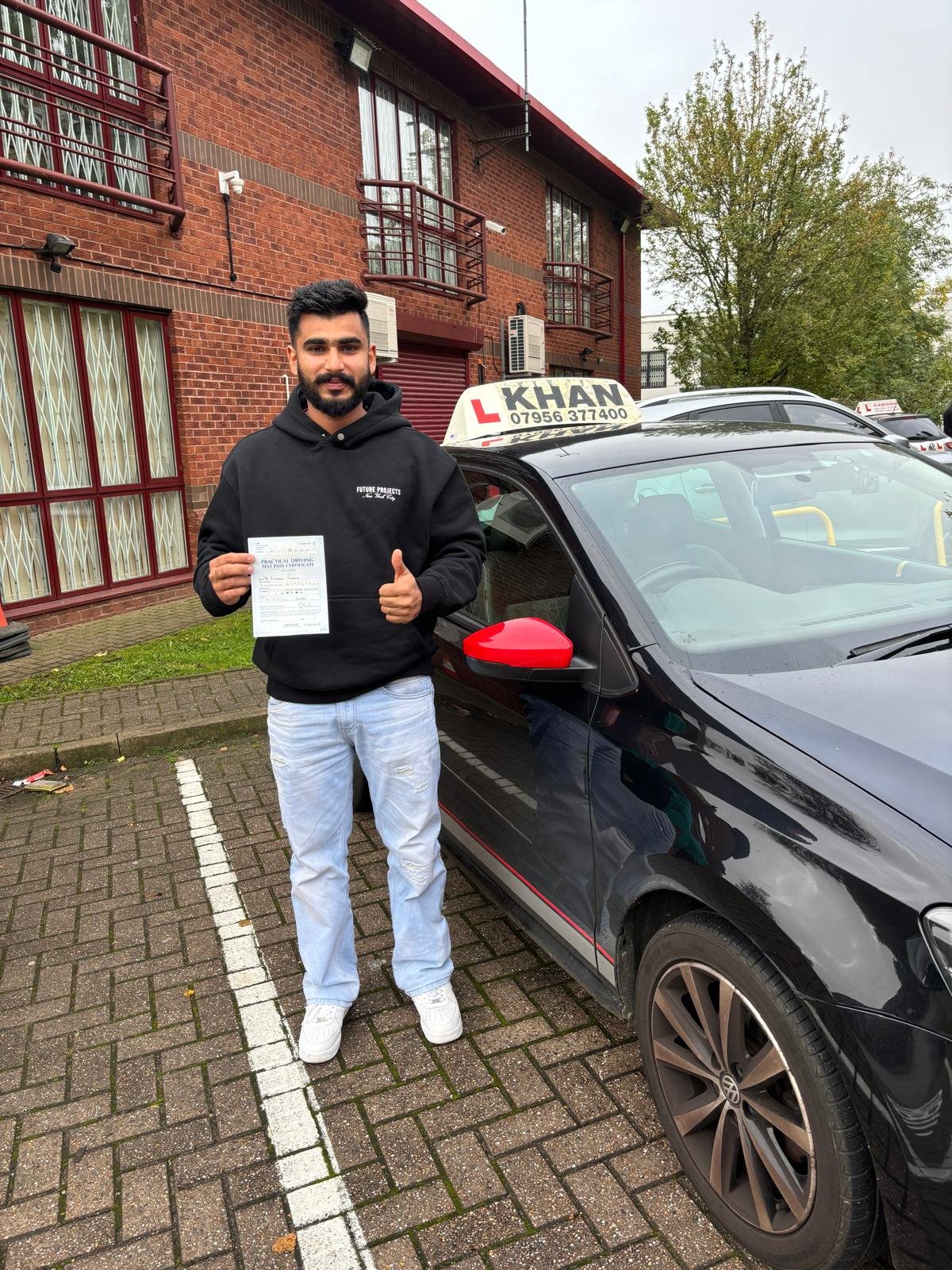 Sunjat holding his driving test pass certificate next to Khan School of Motoring car in Slough