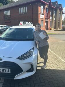 Karen holding her driving test pass certificate next to Khan School of Motoring car in Slough