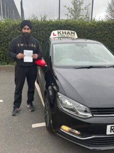 Satpal holding his driving test pass certificate next to Khan School of Motoring car in Slough