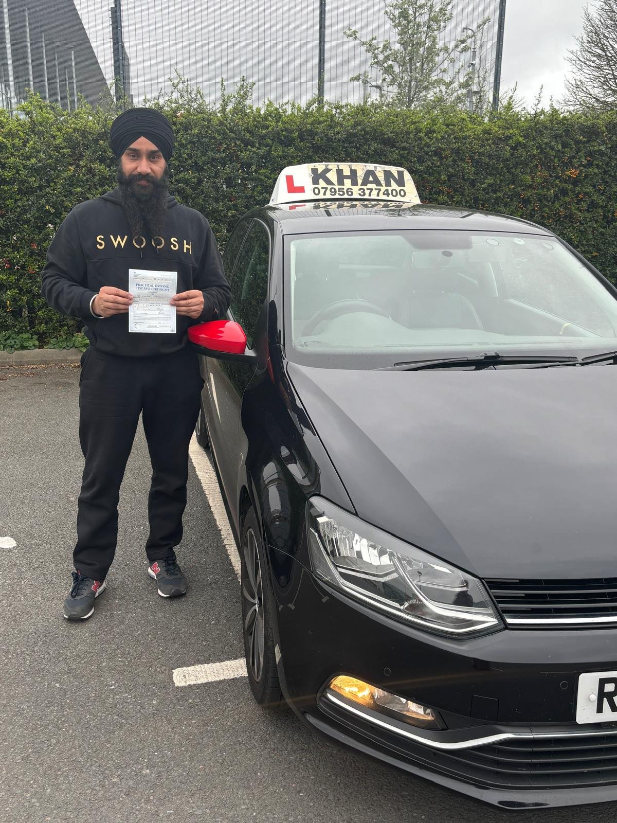 Satpal holding his driving test pass certificate next to Khan School of Motoring car in Slough